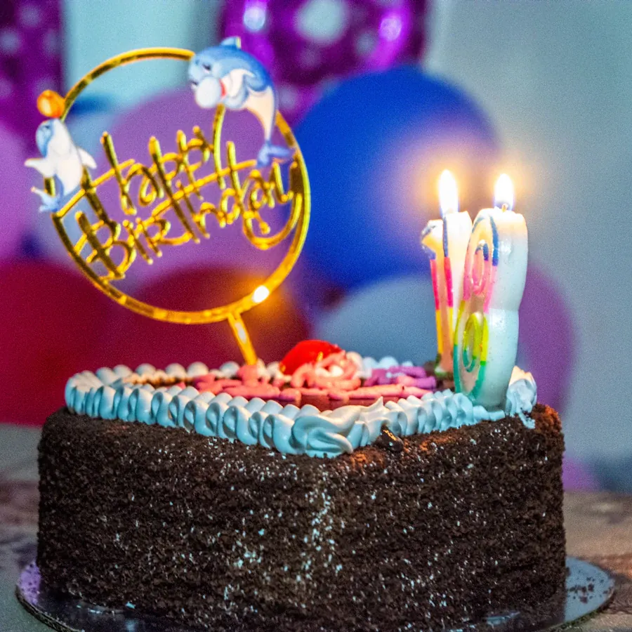 Üzerinde yanan mumlar ve "Happy Birthday" süslemesi olan çikolatalı doğum günü pastası